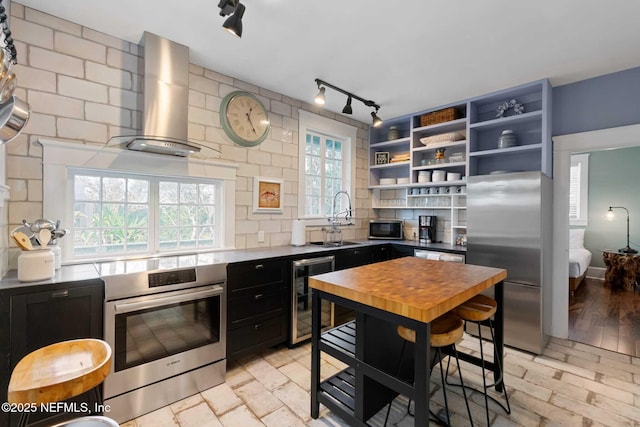 kitchen with sink, tasteful backsplash, stainless steel appliances, beverage cooler, and wall chimney range hood