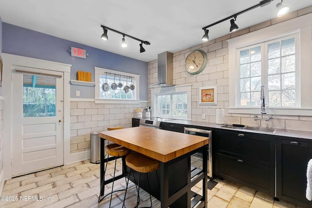 kitchen featuring stainless steel electric range oven, sink, tile walls, a kitchen breakfast bar, and wall chimney range hood