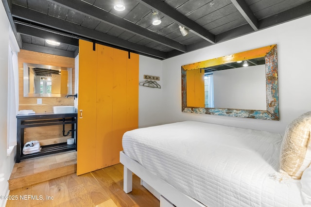 bedroom with wood ceiling, beam ceiling, a barn door, and light wood-type flooring