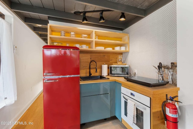 kitchen featuring rail lighting, sink, refrigerator, beam ceiling, and white oven