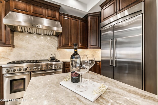 kitchen with high end appliances, tasteful backsplash, ventilation hood, and light stone counters