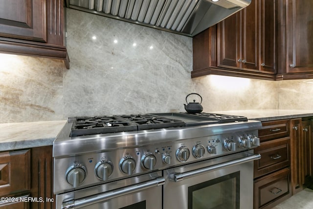 kitchen with tasteful backsplash, dark brown cabinetry, wall chimney exhaust hood, and range with two ovens