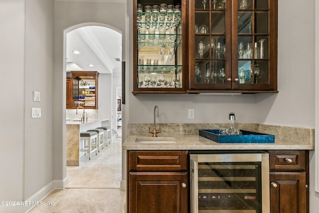 bar featuring sink, beverage cooler, light tile patterned floors, dark brown cabinetry, and light stone counters