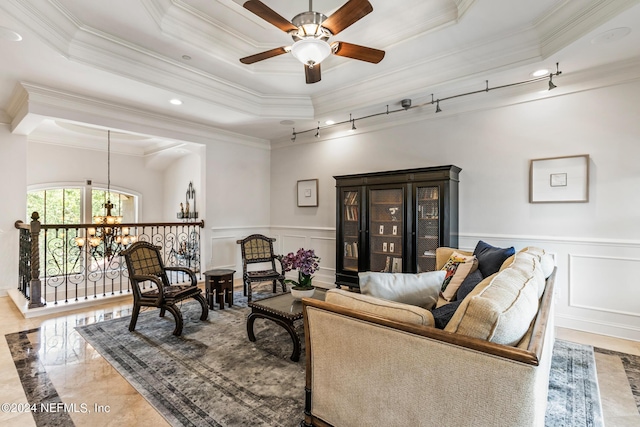 living room with crown molding, ceiling fan with notable chandelier, and a raised ceiling