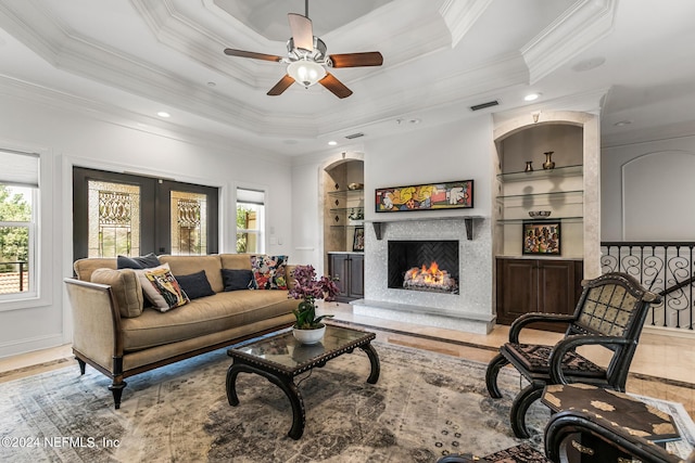 living room with built in shelves, french doors, crown molding, a raised ceiling, and a high end fireplace