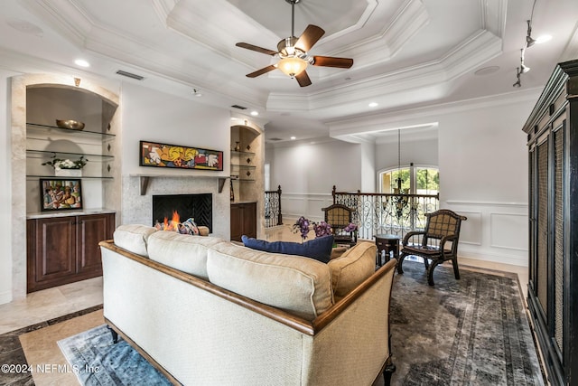 living room featuring built in shelves, ceiling fan, a tray ceiling, and crown molding