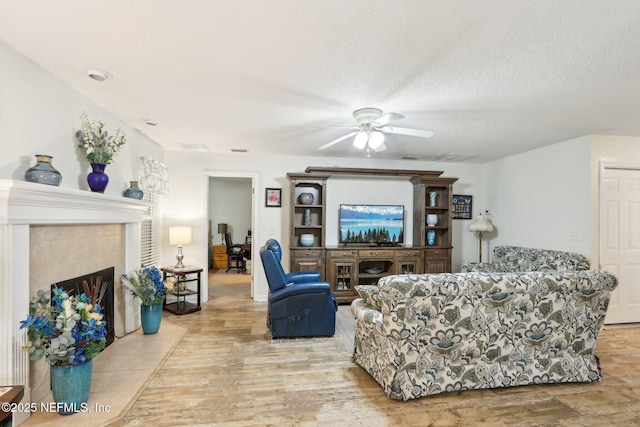 living room featuring a tile fireplace, a textured ceiling, ceiling fan, and light wood-type flooring