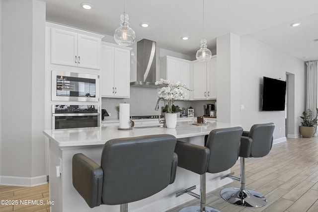 kitchen with white cabinetry, wall chimney range hood, pendant lighting, and stainless steel appliances