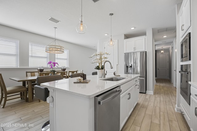 kitchen featuring white cabinetry, an island with sink, sink, hanging light fixtures, and stainless steel appliances