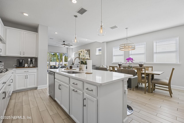 kitchen featuring sink, hanging light fixtures, white cabinets, a center island with sink, and stainless steel dishwasher