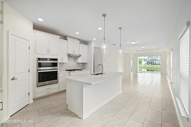 kitchen with a sink, under cabinet range hood, open floor plan, gas stovetop, and stainless steel double oven