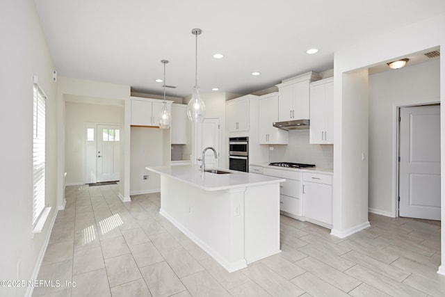 kitchen featuring backsplash, under cabinet range hood, double oven, light countertops, and a sink