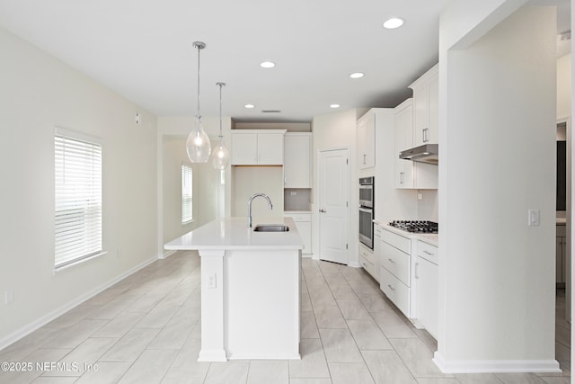 kitchen featuring under cabinet range hood, an island with sink, light countertops, stainless steel appliances, and a sink