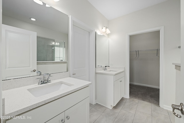 full bathroom with a walk in closet, two vanities, baseboards, and a sink