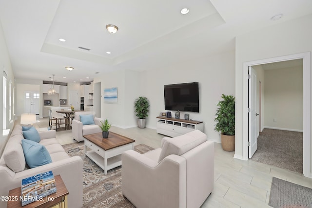 living area with a tray ceiling, recessed lighting, visible vents, and baseboards