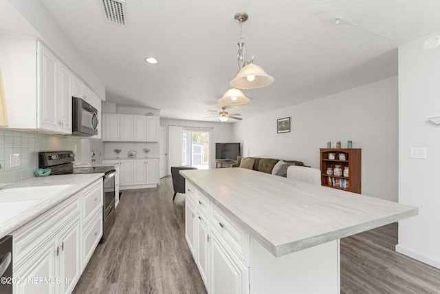 kitchen featuring white cabinetry, decorative light fixtures, a center island, hardwood / wood-style flooring, and stainless steel appliances