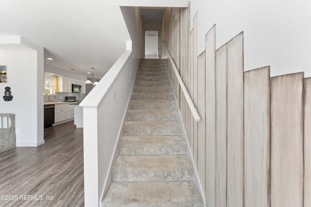 staircase with wood-type flooring, sink, and a textured ceiling