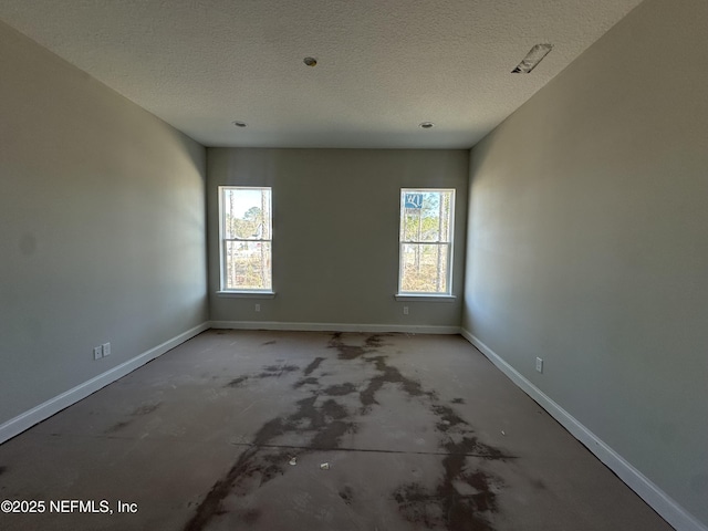 empty room featuring a textured ceiling, concrete flooring, a wealth of natural light, and baseboards