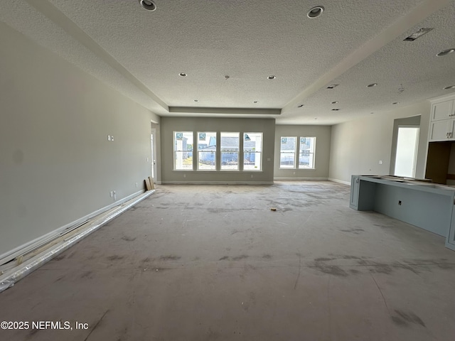 unfurnished living room with baseboards, a raised ceiling, and a textured ceiling