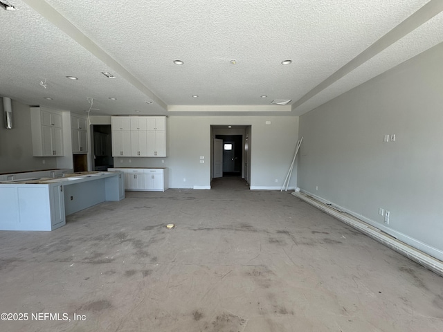 unfurnished living room with a tray ceiling, baseboards, and a textured ceiling