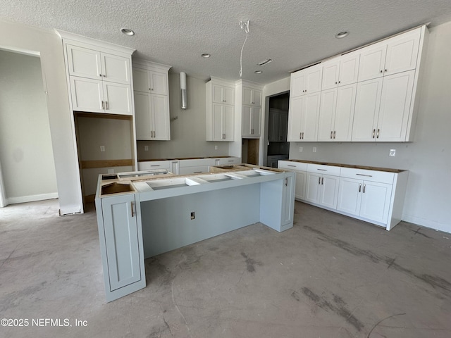 kitchen featuring a center island, white cabinets, concrete floors, and a textured ceiling