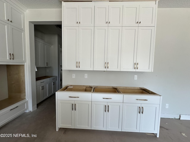 kitchen featuring concrete floors, white cabinets, and a textured ceiling