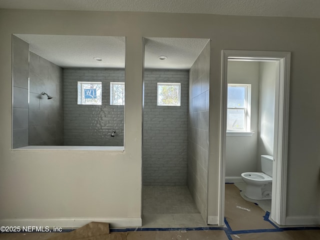 bathroom with a textured ceiling, toilet, walk in shower, and a wealth of natural light