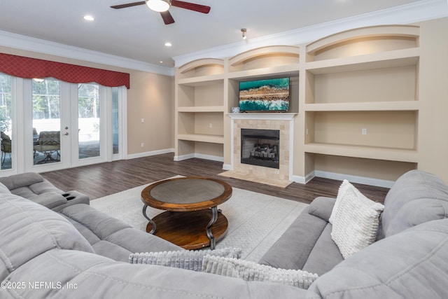 living room featuring hardwood / wood-style floors, a fireplace, ceiling fan, crown molding, and built in shelves