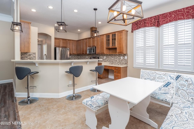 kitchen featuring pendant lighting, a breakfast bar, appliances with stainless steel finishes, tasteful backsplash, and kitchen peninsula