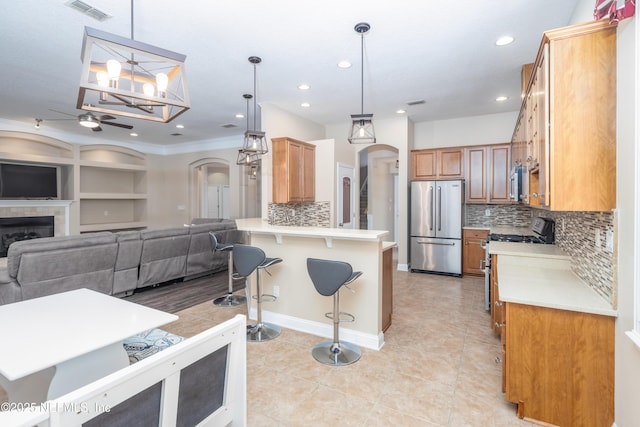 kitchen featuring appliances with stainless steel finishes, a breakfast bar area, hanging light fixtures, a tiled fireplace, and kitchen peninsula