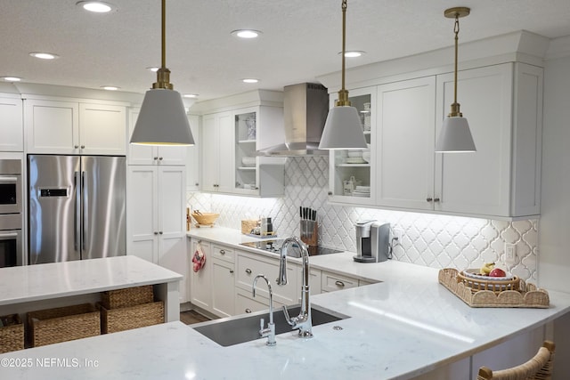 kitchen with appliances with stainless steel finishes, tasteful backsplash, white cabinets, hanging light fixtures, and wall chimney exhaust hood