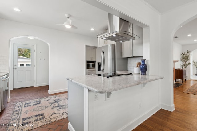 kitchen with a breakfast bar area, appliances with stainless steel finishes, kitchen peninsula, island exhaust hood, and backsplash