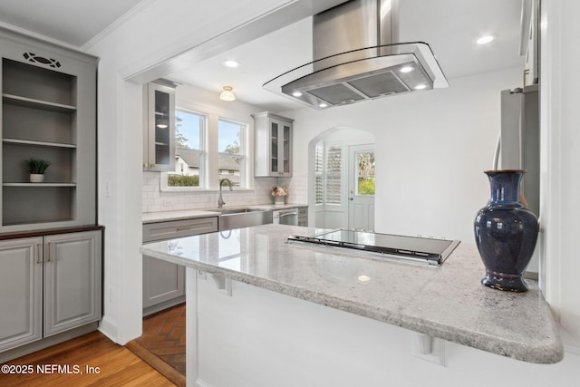 kitchen with sink, a breakfast bar area, light stone counters, island range hood, and backsplash