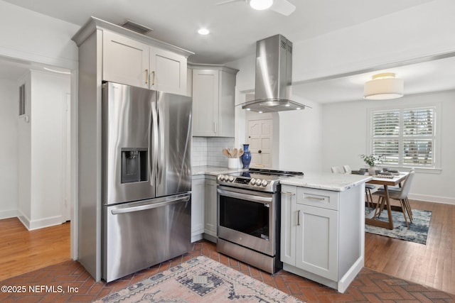 kitchen featuring stainless steel appliances, island range hood, backsplash, and light stone counters