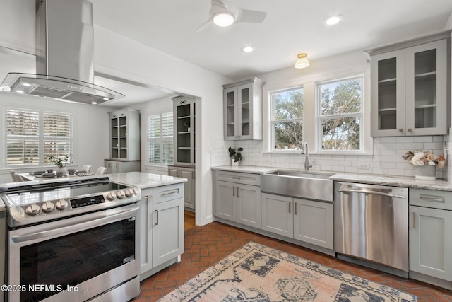 kitchen featuring island exhaust hood, appliances with stainless steel finishes, light stone countertops, and sink