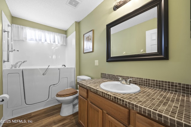 bathroom with vanity, a bath, wood-type flooring, a textured ceiling, and toilet