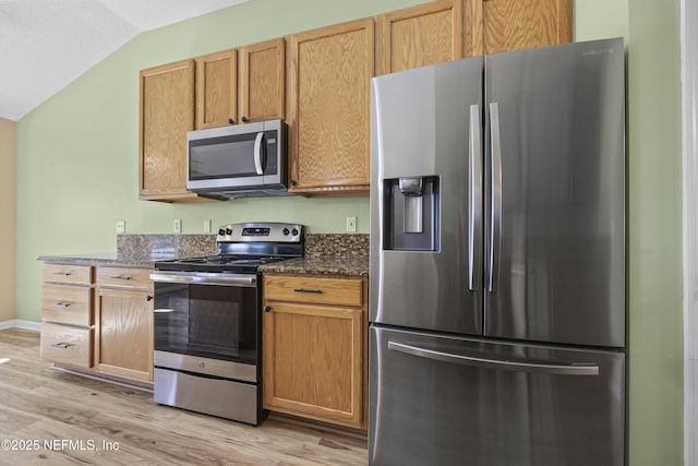 kitchen with stainless steel appliances, lofted ceiling, dark stone countertops, and light wood-type flooring