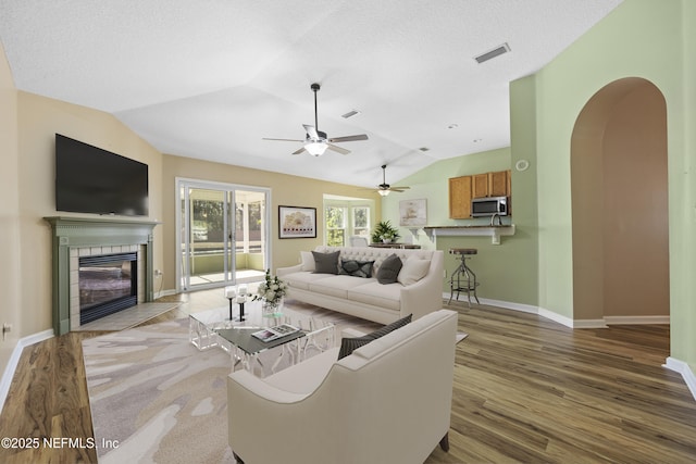 living room featuring a textured ceiling, vaulted ceiling, a tile fireplace, and wood-type flooring