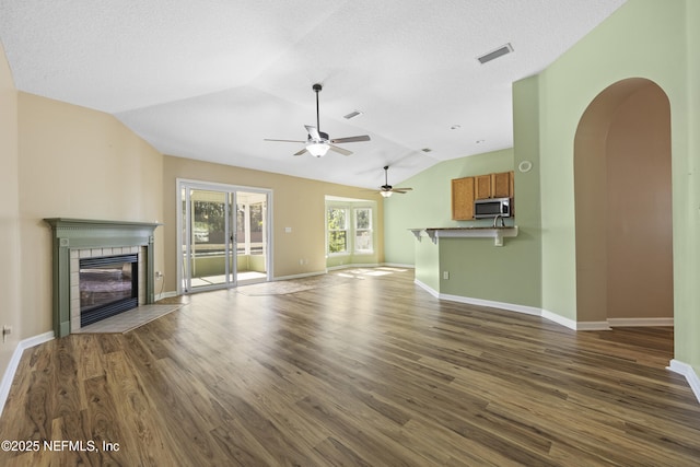 unfurnished living room featuring lofted ceiling, dark hardwood / wood-style flooring, ceiling fan, a textured ceiling, and a tiled fireplace