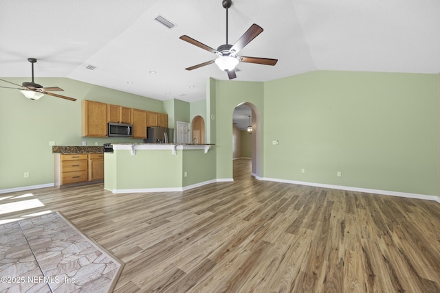 kitchen with vaulted ceiling, appliances with stainless steel finishes, a breakfast bar area, ceiling fan, and light hardwood / wood-style flooring