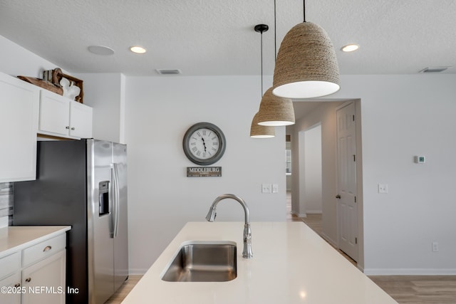 kitchen with a sink, decorative light fixtures, white cabinetry, stainless steel fridge with ice dispenser, and light countertops