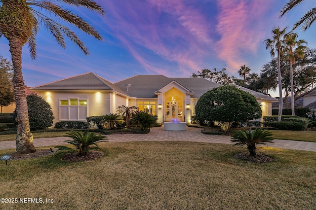 view of front facade with decorative driveway, a tiled roof, a front lawn, and stucco siding