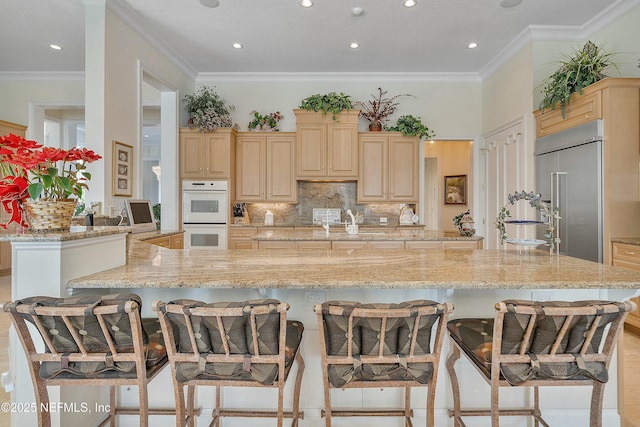 kitchen with light brown cabinetry, a kitchen bar, white double oven, and built in refrigerator