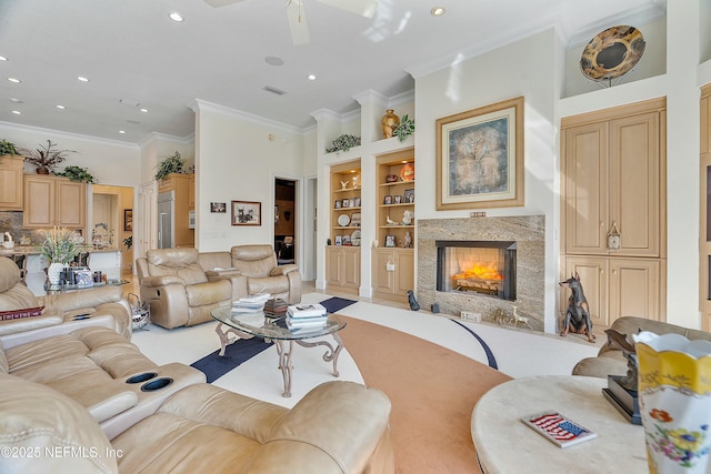 living room featuring ornamental molding, ceiling fan, a fireplace, and built in shelves