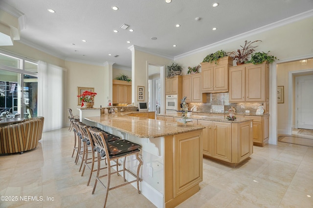 kitchen with a large island, a breakfast bar area, white oven, light stone counters, and light brown cabinetry