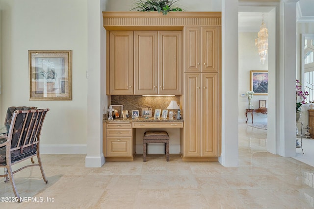 kitchen featuring built in desk, light brown cabinetry, a chandelier, decorative backsplash, and light stone counters