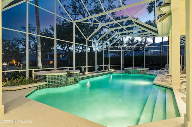 pool at dusk featuring an in ground hot tub, a patio, and glass enclosure