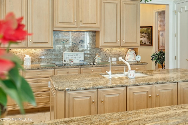 kitchen featuring black electric cooktop, sink, tasteful backsplash, and light stone countertops