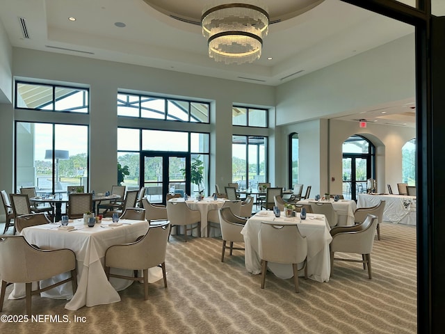 dining space with a tray ceiling, plenty of natural light, carpet flooring, and a towering ceiling