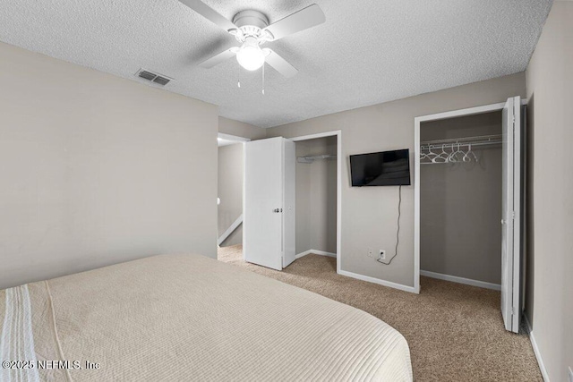 bedroom featuring multiple closets, ceiling fan, light colored carpet, and a textured ceiling